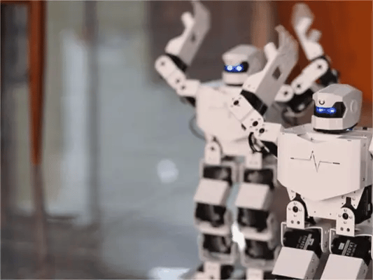 Two white H5S humanoid robots performing a raised-arm dance pose