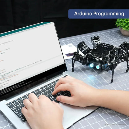 Hexapod robot beside a laptop displaying Arduino programming code